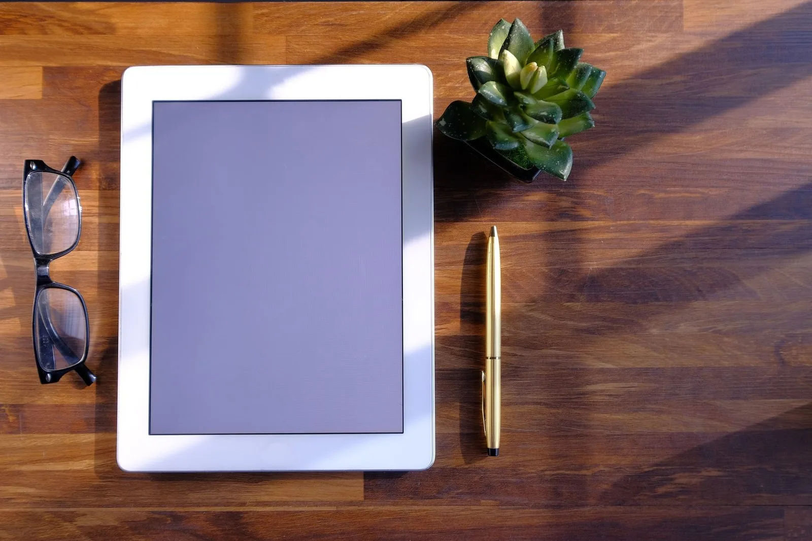 Tablet sobre un escritorio de madera junto a anteojos y una planta, lista para estudiar o leer